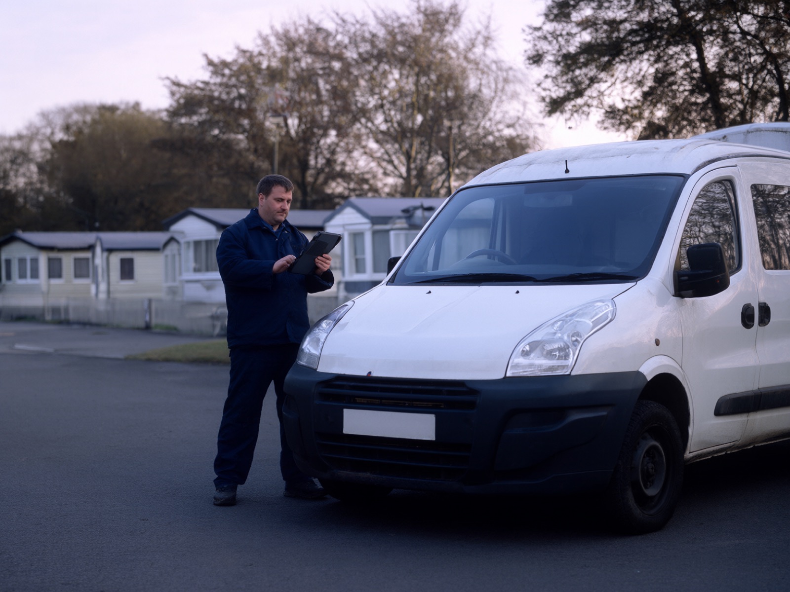 A maintenance worker checking a tablet beside a white van on a holiday park road